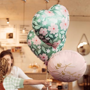 May include: Three heart-shaped balloons with floral patterns. Two balloons are green with pink flowers and one balloon is pink with gold lettering that says "Kochmam Cie Mama".