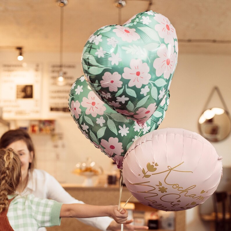 May include: Three heart-shaped balloons with floral patterns. Two balloons are green with pink flowers and one balloon is pink with gold lettering that says "Kochmam Cie Mama".