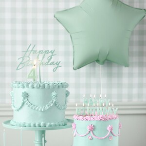 May include: Two pastel green birthday cakes with pink frosting and candles. One cake has a single candle with the number "4" on it and the other cake has candles that spell out "Happy Birthday".