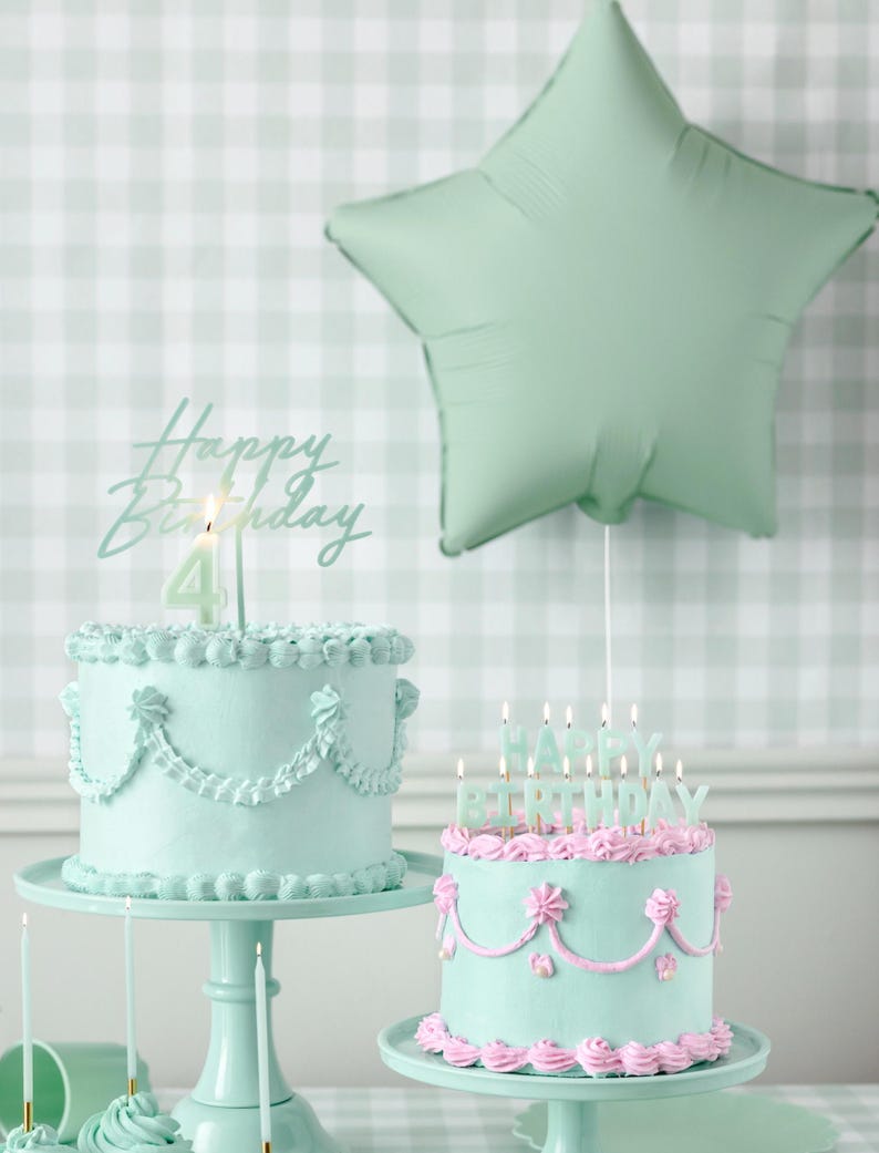 May include: Two pastel green birthday cakes with pink frosting and candles. One cake has a single candle with the number "4" on it and the other cake has candles that spell out "Happy Birthday".