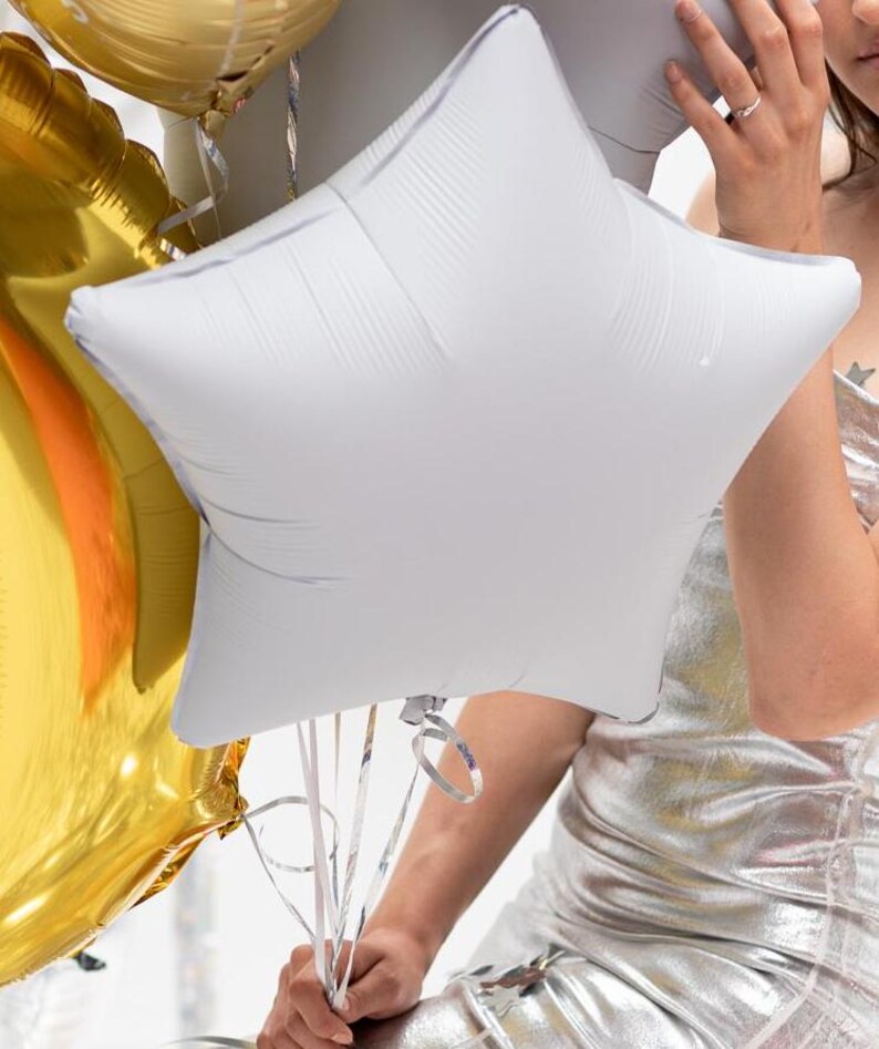 Op de afbeelding: Een zilveren stervormige ballon die door een persoon in een zilveren jurk wordt vastgehouden. De ballon is vastgebonden met witte linten.