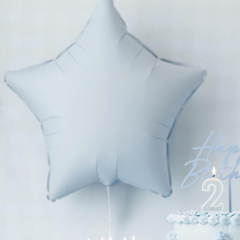 May include: A light blue star-shaped balloon with a cake in the background. The cake is decorated with blue frosting and a number two candle.