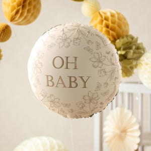 Puede incluir: Un globo redondo, blanquecino, con las palabras "OH BABY" en letras marrones, rodeado de un dise&ntilde;o floral. El globo es parte de una decoraci&oacute;n de baby shower o guarder&iacute;a, con otros elementos decorativos en el fondo.