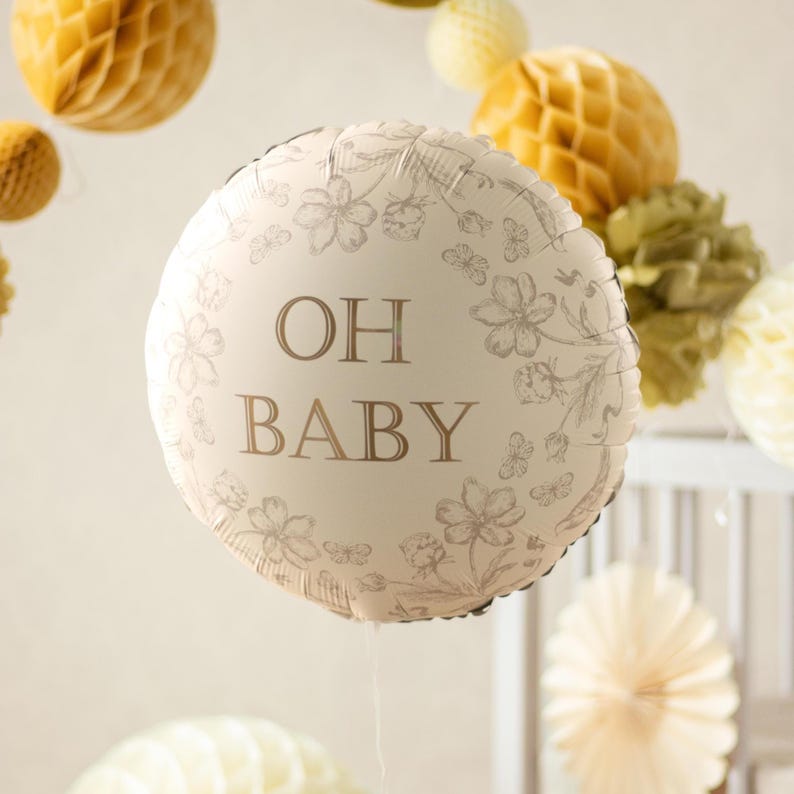 Puede incluir: Un globo redondo, blanquecino, con las palabras "OH BABY" en letras marrones, rodeado de un dise&ntilde;o floral. El globo es parte de una decoraci&oacute;n de baby shower o guarder&iacute;a, con otros elementos decorativos en el fondo.