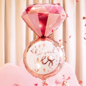 May include: A rose gold foil balloon shaped like a ring with a diamond on top. The ring balloon has the text "She said yes" on it.