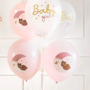 May include: A set of pink and white balloons with gold lettering and illustrations of a bear sleeping on a crescent moon. The balloons say "Baby girl" and "Baby girl".