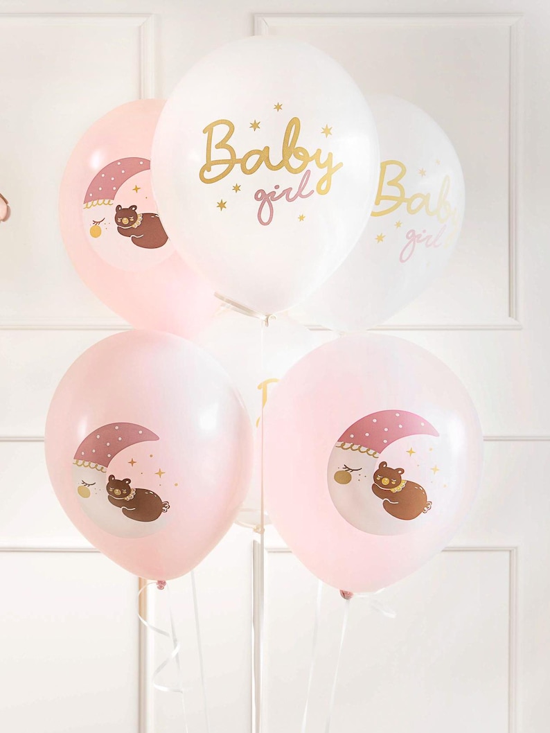 May include: A set of pink and white balloons with gold lettering and illustrations of a bear sleeping on a crescent moon. The balloons say "Baby girl" and "Baby girl".