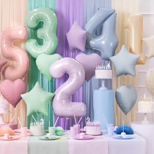 Puede incluir: Globos de colores pastel en forma de n&uacute;meros 2, 3, 4 y 5, junto con estrellas y corazones, decoran una mesa con pasteles y otras decoraciones de fiesta.