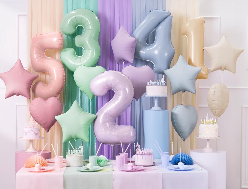 Puede incluir: Globos de colores pastel en forma de n&uacute;meros 2, 3, 4 y 5, junto con estrellas y corazones, decoran una mesa con pasteles y otras decoraciones de fiesta.