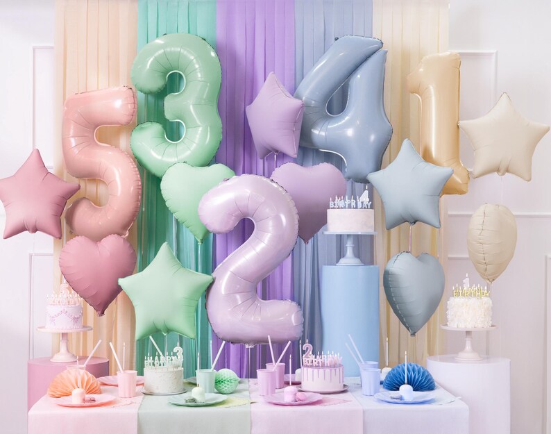 May include: A pastel-colored birthday party decoration set with foil balloons in the shape of numbers 1, 2, 3, 4, and 5, stars, and hearts. The balloons are arranged in front of a backdrop of pastel-colored streamers.