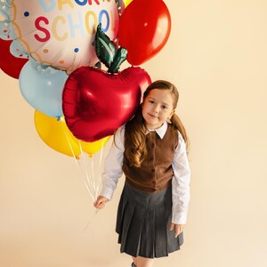 Child holding a red apple foil balloon for back to school party and classroom decoration