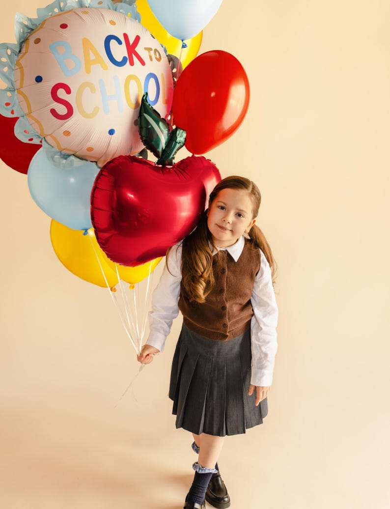 Child holding a red apple foil balloon for back to school party and classroom decoration
