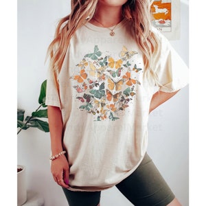 May include: A beige oversized t-shirt with a graphic print of colorful butterflies. The shirt is worn with dark green biker shorts.