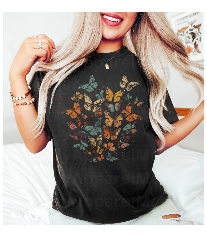 May include: Black t-shirt with a colorful butterfly graphic print. The butterflies are arranged in a cluster and are in various shades of orange, yellow, blue, and green.