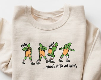 May include: A beige sweatshirt with a green and orange cartoon character graphic. The character is shown in a series of poses with the text "ohh" and "whhuuu" above the character. The text "...that's it I'm not going" is below the character.