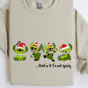 Może przedstawiać: Beżowa bluza z nadrukiem świątecznym przedstawiającym cztery zielone postacie Stitchów w czapkach Świętego Mikołaja. Pod postaciami znajduje się napis "...that's it I'm not going".
