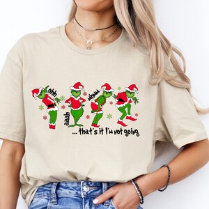 Może przedstawiać: Beżowa koszulka z nadrukiem Grincha w czapce Świętego Mikołaja, który mówi "...that's it I'm not going."