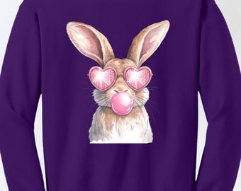 May include: Purple sweatshirt with a cartoon illustration of a brown rabbit wearing pink heart-shaped sunglasses and blowing a pink bubble.