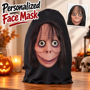 Pode incluir: Uma máscara facial de tecido preto com um gráfico impresso de um personagem pálido de olhos arregalados, cabelos escuros longos e um sorriso largo. O texto Personalized Face Mask está impresso em letras pretas e vermelhas acima.