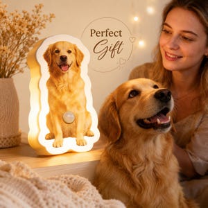 May include: A white, dog-shaped LED night light featuring a printed image of a golden retriever sitting down. The lamp has a circular power button on the front and emits a warm, soft glow. The text "Perfect Gift" is printed above the lamp.