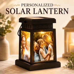 May include: A black solar lantern featuring a square frame with a top solar panel and a handle. The lantern displays a photographic print of a family on its side panels, illuminated from within by a warm light. Text above reads PERSONALIZED SOLAR LANTERN.