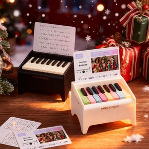 May include: Two miniature piano calendars, one black and one white, sit on a wooden surface. The black piano has white keys, while the white piano has colorful keys. Each calendar displays a music sheet and a small screen with a family photo. The text "PIANO CALENDAR" is visible.