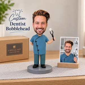 May include: A custom dentist bobblehead featuring a figure with brown hair wearing a teal tunic and pants, holding a pair of black dental forceps with a white tooth. Next to it is a framed photograph of the same person and a cardboard gift box.