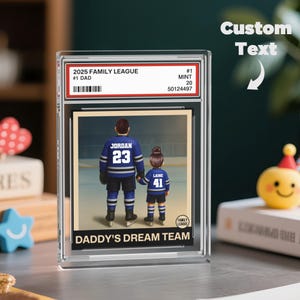 May include: A clear acrylic display case with a hockey-themed image. The image depicts a father and child in hockey jerseys, with the text "DADDY'S DREAM TEAM." The case also includes the text "2025 FAMILY LEAGUE" and "#1 DAD."