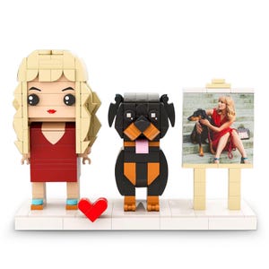 May include: A Lego-style display featuring a blonde woman, a Rottweiler dog, and a framed photo. The woman wears a red dress and the dog is black and brown. A red heart is on the base. The photo shows a woman in a red dress with a dog.