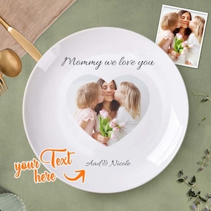 May include: White ceramic plate with a heart-shaped photo of a mother and two children. The text "Mommy we love you" is printed on the plate. The text "your text here" is written in orange below the photo.