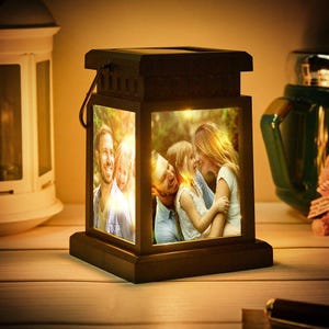 May include: A brown wooden photo lantern with a solar panel on the top. The lantern has two windows with photos of a family inside. The lantern is lit up and glowing.