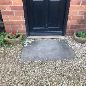 May include: Two stone planters with red and purple flowers, sitting on a gravel path in front of a black door.