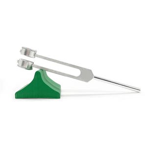 May include: A silver tuning fork with two prongs resting on a green foam wedge. The tuning fork is used for sound therapy and relaxation.