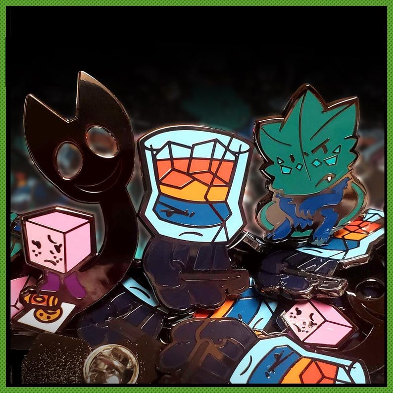 Puede incluir: Una colecci&oacute;n de pines de esmalte met&aacute;lico con varios personajes y objetos. Se incluyen una figura de silueta oscura, un personaje de cubo rosa, un vaso lleno de l&iacute;quido naranja y azul, y una criatura verde azulada con un dise&ntilde;o angular.
