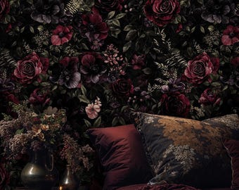Op de afbeelding: Een donkere slaapkamer met bloemenbehang met dieprode rozen en andere bloemen. Een bed met bordeauxrood beddengoed, kussens en een gebreide sprei staat op de voorgrond. Een vaas met bloemen en een kaars staan op een houten nachtkastje.