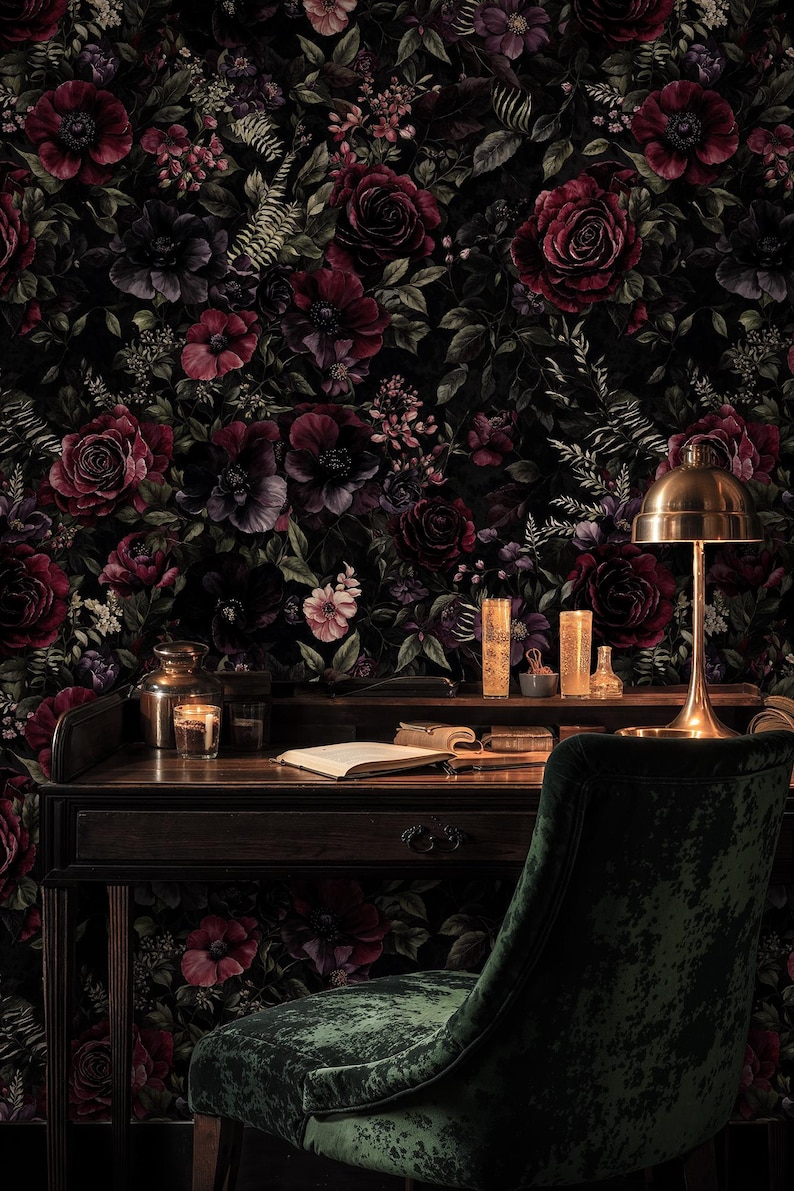 May include: A dark, moody interior scene featuring a wooden desk with a brass lamp, candles, and an open book. The background is a floral wallpaper with deep red and purple roses. A green velvet chair completes the scene.