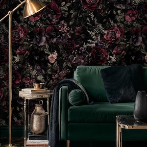 May include: A living room scene featuring a dark green velvet sofa with gold legs, a side table, and a floor lamp. The backdrop is a floral wallpaper with dark red roses and other flowers. A black rug and throw pillows complete the decor.