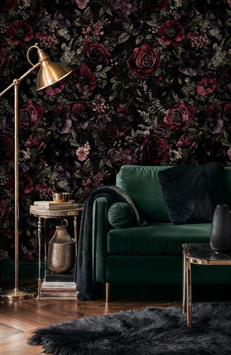 May include: A living room scene featuring a dark green velvet sofa with gold legs, a side table, and a floor lamp. The backdrop is a floral wallpaper with dark red roses and other flowers. A black rug and throw pillows complete the decor.