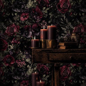 May include: A dark, moody still life featuring lit burgundy candles of varying heights on a rustic wooden surface. The background is a floral wallpaper with deep red and purple roses and foliage. A vintage vase and books are also present.