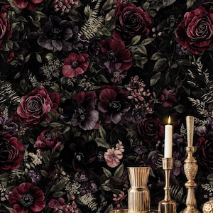 May include: Dark floral wallpaper featuring burgundy and purple roses, anemones, and other flowers against a black background. A gold vase, candle holders, and a lit candle sit on a dark table, adding a touch of elegance.