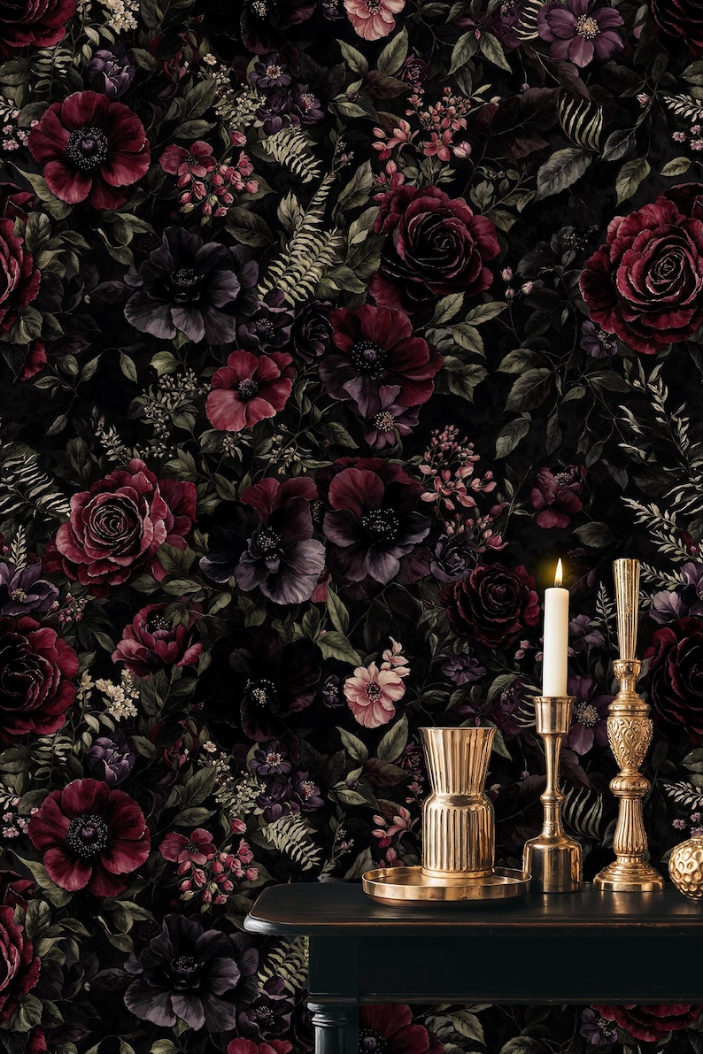 May include: Dark floral wallpaper featuring burgundy and purple roses, anemones, and other flowers against a black background. A gold vase, candle holders, and a lit candle sit on a dark table, adding a touch of elegance.