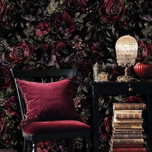 May include: A dark, floral wallpaper featuring burgundy and dark purple roses and other flowers. A black chair with a burgundy velvet cushion and seat is in front of the wallpaper. A small black table holds a lamp and books.