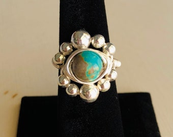 May include: A silver ring with a turquoise stone set in a cluster of silver beads.