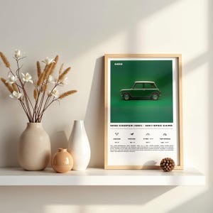 Puede incluir: Impresión enmarcada con un Mini Cooper verde (1961) sobre un fondo verde. La impresión incluye la palabra «MINI» en la parte superior y una tarjeta de especificaciones con detalles del vehículo. En una estantería blanca con jarrones decorativos y una piña.