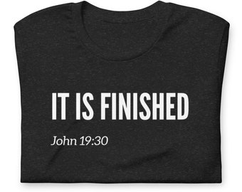 Può includere: T-shirt grigio scuro con la scritta bianca "IT IS FINISHED" a caratteri grandi. Sotto, in bianco e più piccolo, c'è "John 19:30". La maglietta è piegata con cura.