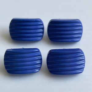 May include: Four blue plastic buttons with a ribbed texture. The buttons are rectangular in shape.