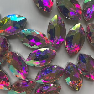 May include: A collection of iridescent marquise-shaped rhinestones. The gems display a spectrum of colors, including pink, purple, green, and yellow, with a metallic silver setting. These decorative embellishments are ideal for crafting and jewelry making.