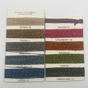 May include: A color card with yarn samples in various shades of brown, red, green, and blue. The card is labeled "DUNE" and includes the names and numbers of each color, such as "Oatmeal 65", "Heather 76", "Strawberry 109", "Coffee 17", "Walnut 48", "Granite 31", "Khaki 90", "Moorland 112", "Camouflage 113", and "Cloud 111".
