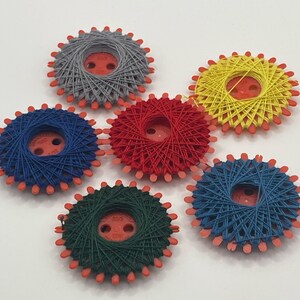 以下が含まれることがあります： 赤、青、緑、黄、グレーなど、さまざまな色の糸巻きが6つあります。糸巻きはプラスチック製で、星形のデザインです。各糸巻きには、中央に小さなボタンが付いています。