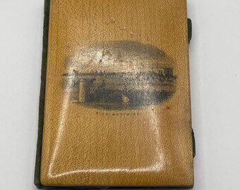 May include: A small wooden book with a green fabric cover. The front cover features a black and white illustration of a horse race with the text "The Weathring" underneath.
